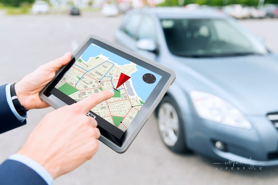 man's hands holding a GPS tracker in front of silver car