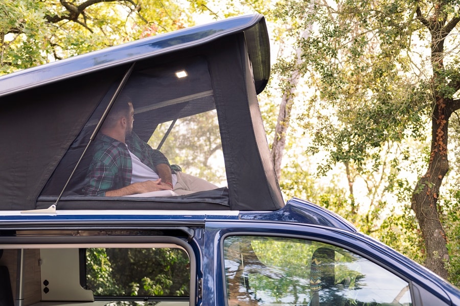 man lying in the pop-up tent of his camper van